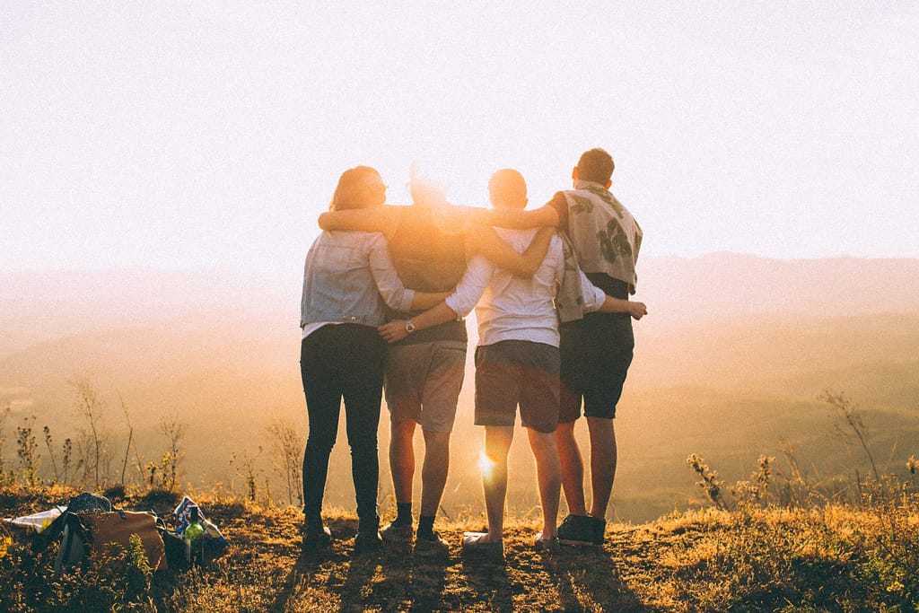 Four people with arms around eachother looking ahead towards the sun