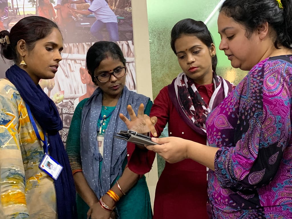 Four Operation ASHA team members looking at a tablet and pointing at different features of the prototype app