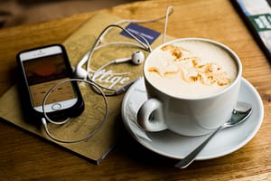 flatlay of phone with headphones and cup of coffee