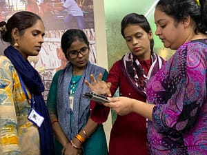 Four Operation ASHA employees looking at a tablet and pointing at and discussing different features