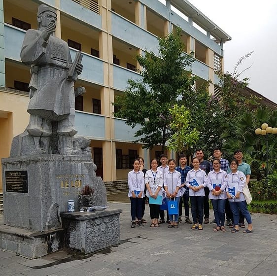 HOCMAI students, staff, and volunteer Sam posing in front of a school in Vietnam